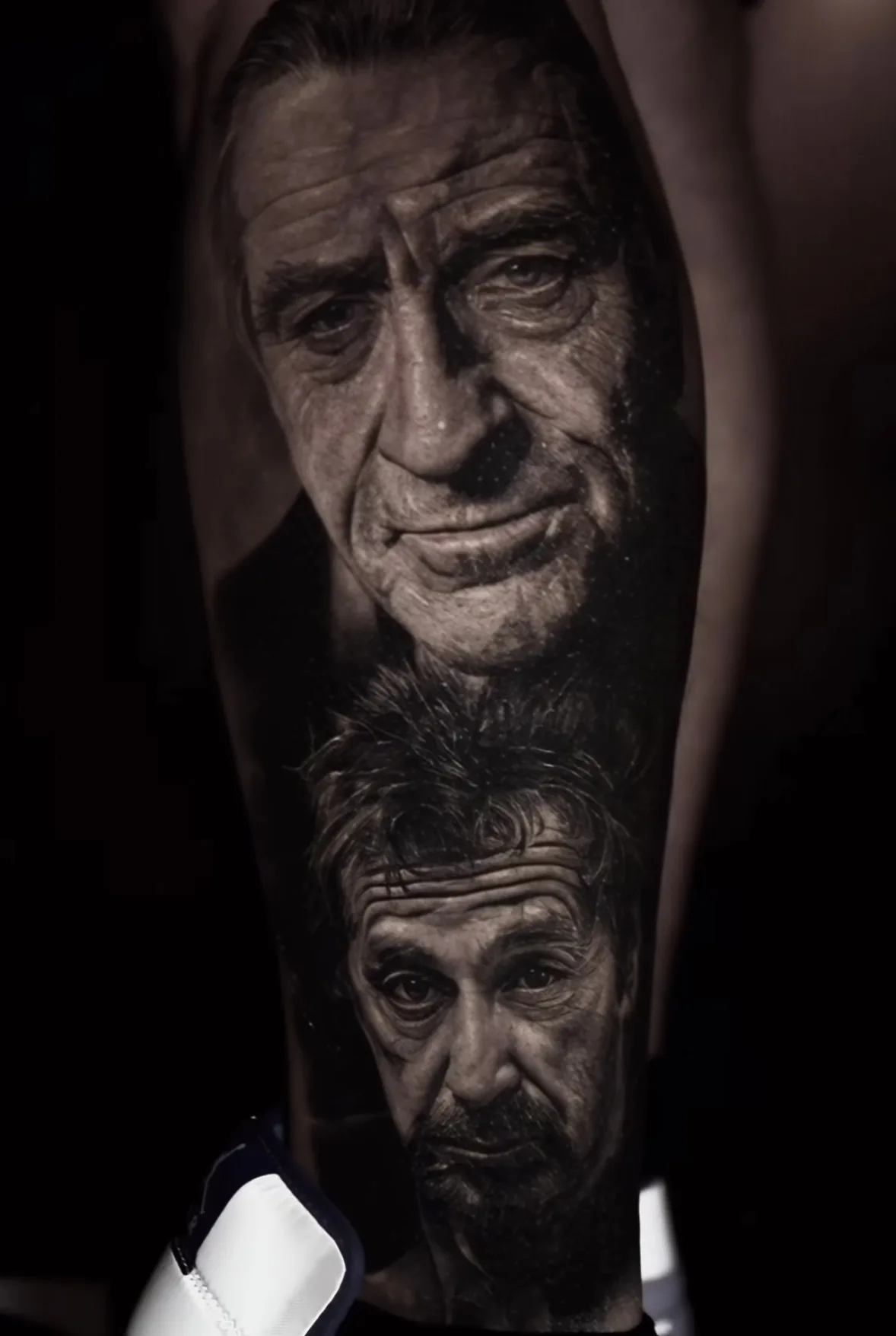 Two expressive male portraits in a black and grey tattoo.