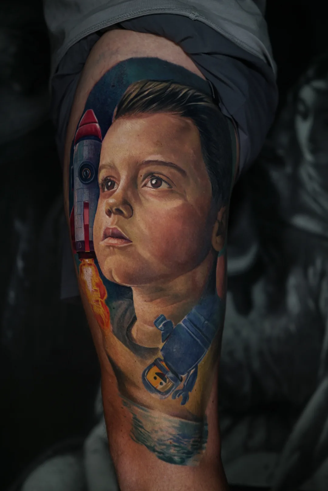 A child’s portrait with a rocket and space imagery, tattooed in colour.