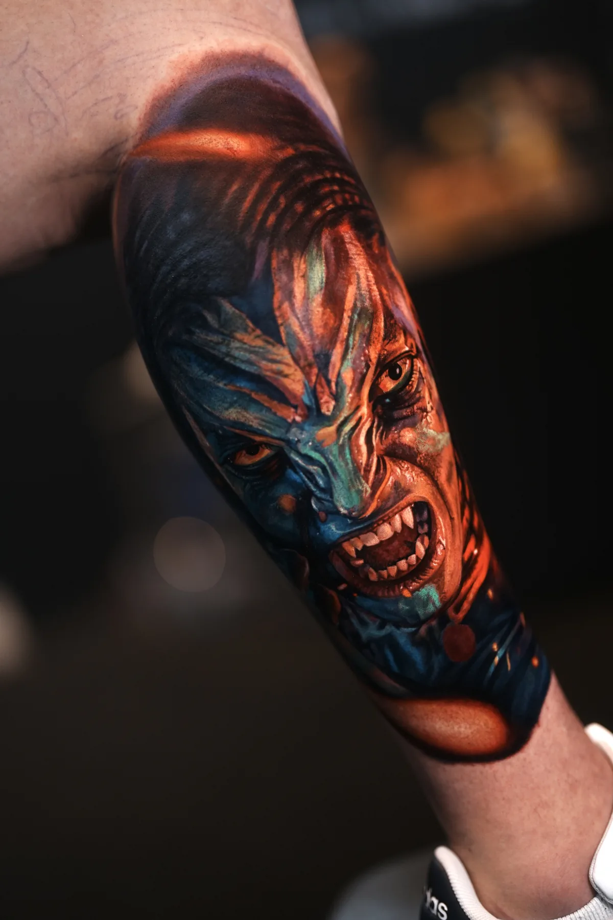 A blue and red face with bared teeth, tattooed on an arm.