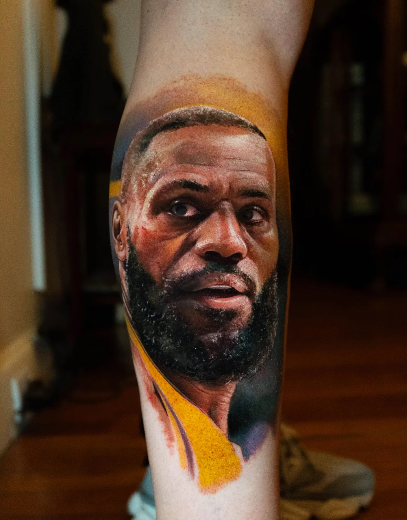 A close-up portrait tattoo of a basketball player in a gold jersey.