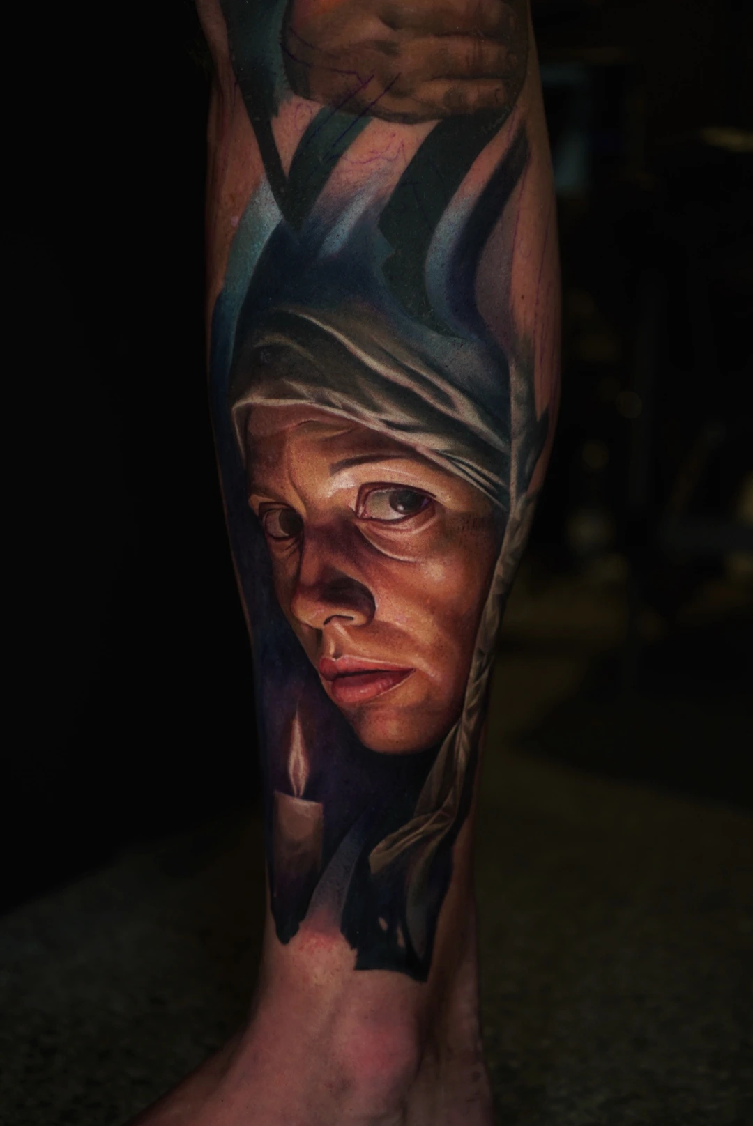 A colour-realism portrait of a woman in a dark blue veil, tattooed on a lower leg.