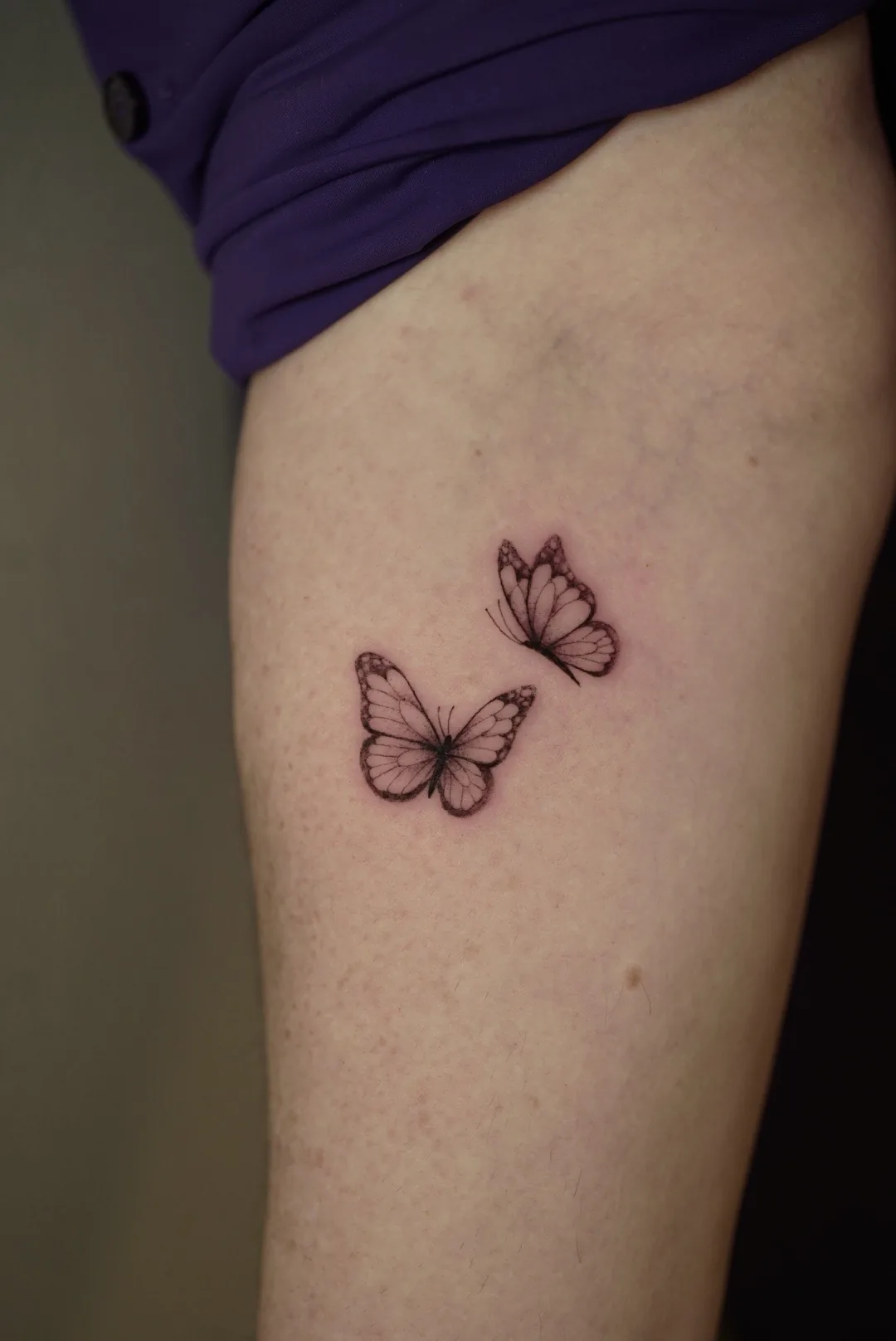 Two small butterflies tattooed with delicate outlines.