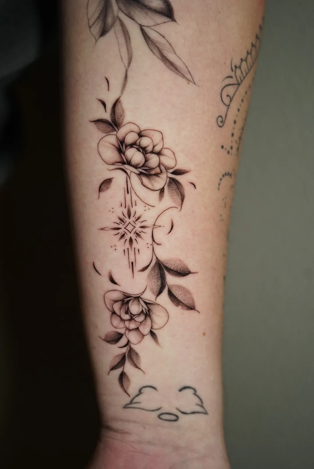 A vertical arrangement of flowers and leaves tattooed on a forearm.