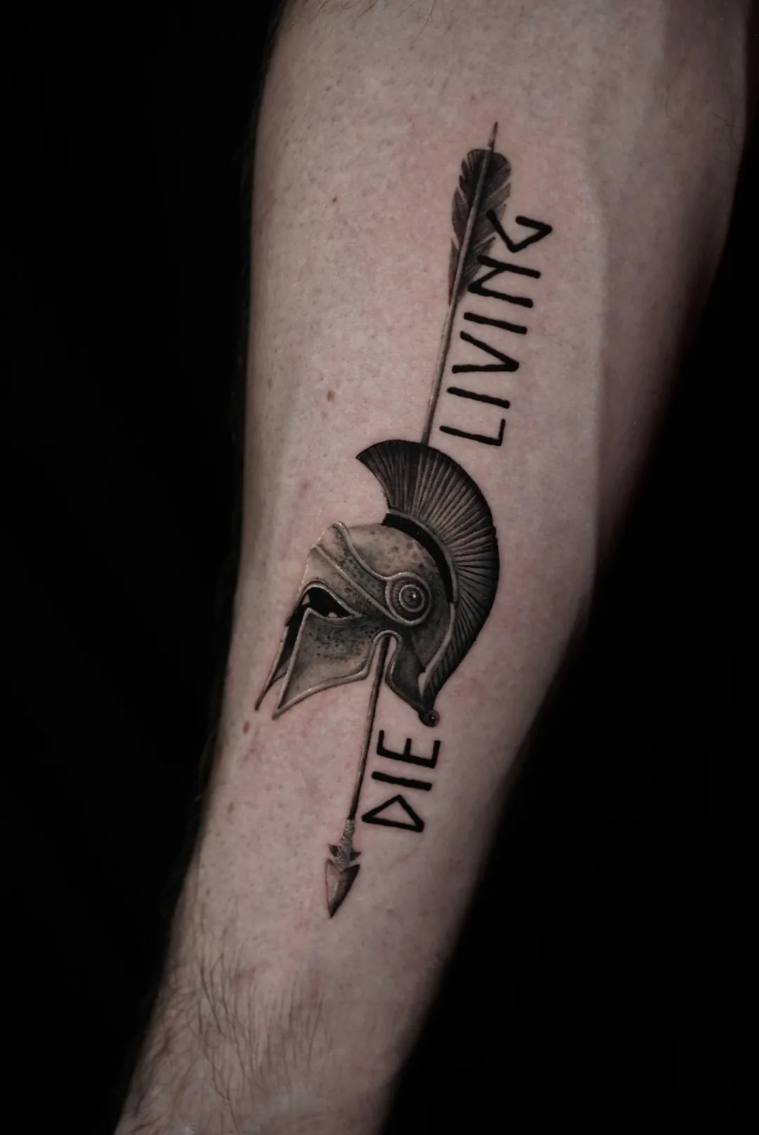 A crested helmet and arrow with vertical lettering, tattooed in black and grey.