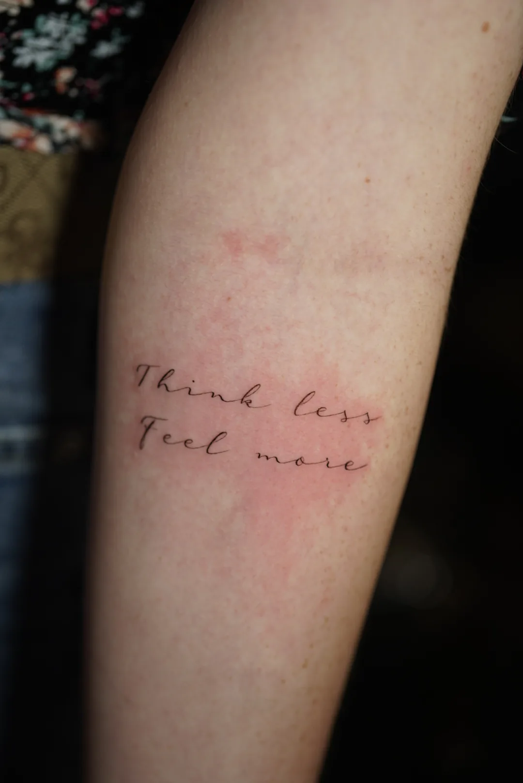 The words Think less, Feel more in delicate handwritten tattoo lettering.